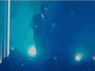a man in a suit is dancing in a dark room with blue lights