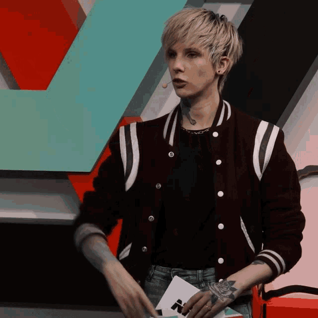 a woman with short blonde hair is wearing a maroon and white jacket