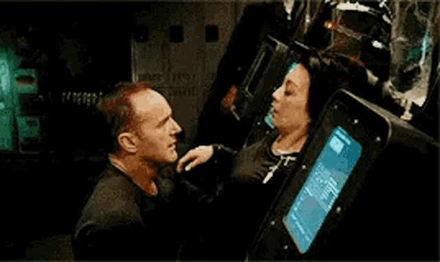 a man and a woman are standing next to each other in front of a computer monitor .