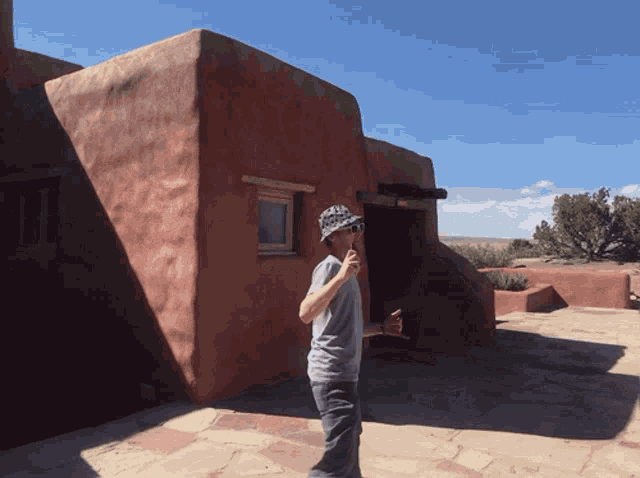 a man wearing a hat and sunglasses stands in front of a building