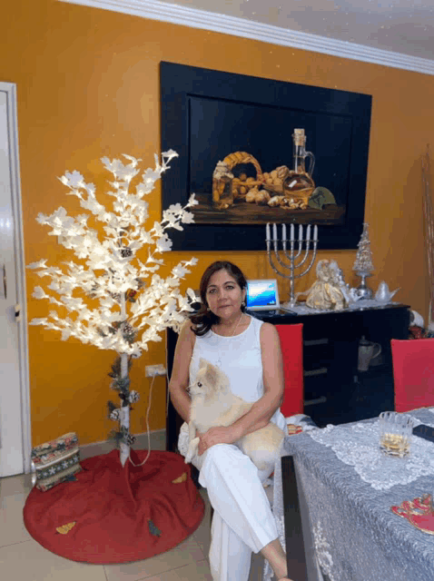 a woman sits at a table holding a small dog in front of a christmas tree