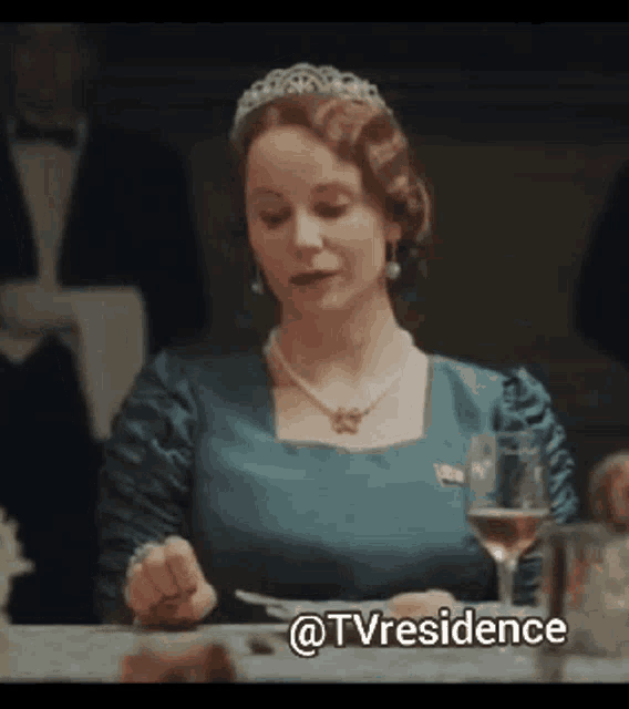 a woman in a blue dress and tiara sits at a table