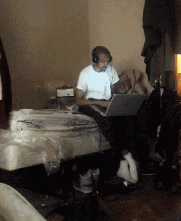 a man wearing headphones sits on a bed using a laptop computer