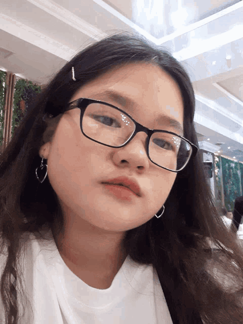 a young girl wearing glasses and a white shirt looks at the camera