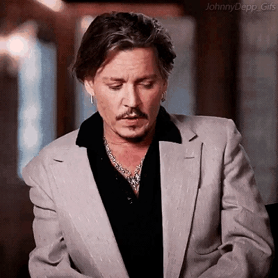 johnny depp is wearing a suit and a black shirt and is looking down .