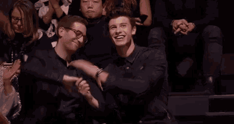 two men are sitting next to each other in a crowd of people .