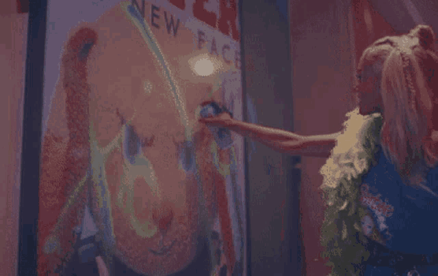 a woman touches a barbie doll 's face in front of a sign that says new face