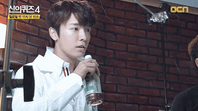 a man holding a bottle in front of a brick wall that says ocn on the bottom
