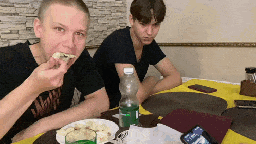 two young men sitting at a table with a bottle of sprite