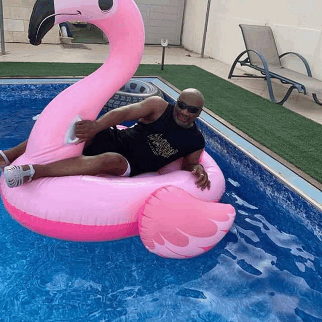 a bald man is laying on a pink flamingo float in a pool