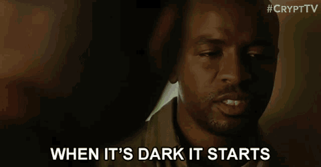 a man is talking to another man in a dark room while another man looks on .