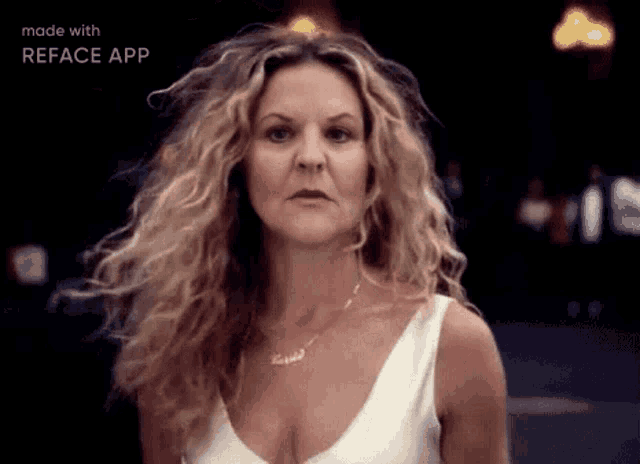 a woman with curly hair is wearing a white tank top and necklace .