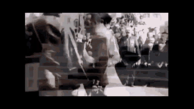 a black and white photo of a man standing in front of a crowd .