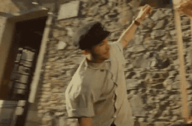 a man wearing a baseball cap is standing in front of a stone wall and holding something in his hand .