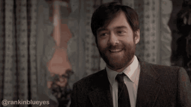 a man with a beard wearing a suit and tie is smiling