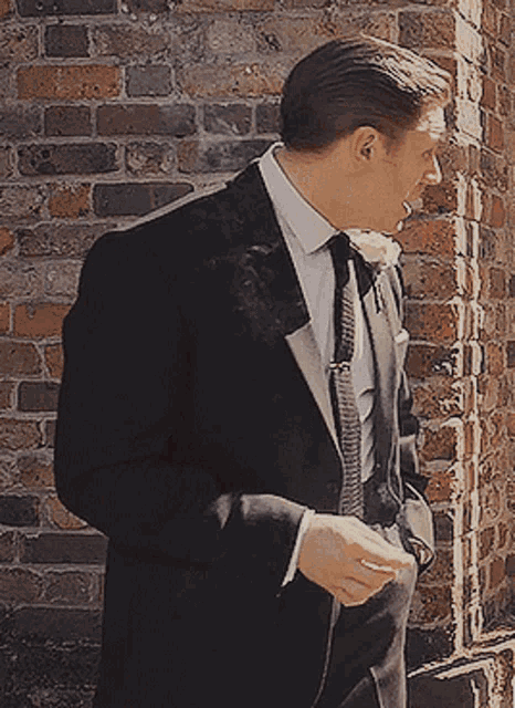 a man in a suit and tie standing in front of a brick wall