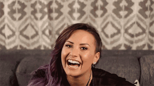 a woman with purple hair is sitting on a couch and smiling .