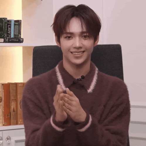 a man wearing a brown sweater is clapping his hands in front of a shelf of books including one titled law