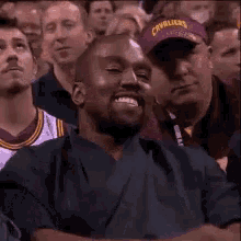 a man with a beard is sitting in a crowd of people watching a game .