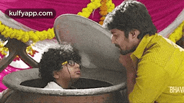 a man in a yellow shirt is standing next to a boy in a pot with the lid open .