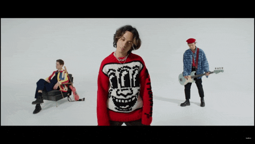 a man in a red sweater with a smiley face on it stands in front of two other men