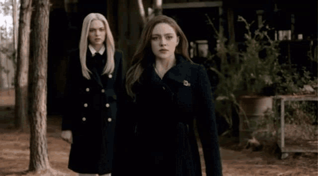 two women in black coats are standing next to each other in the woods .
