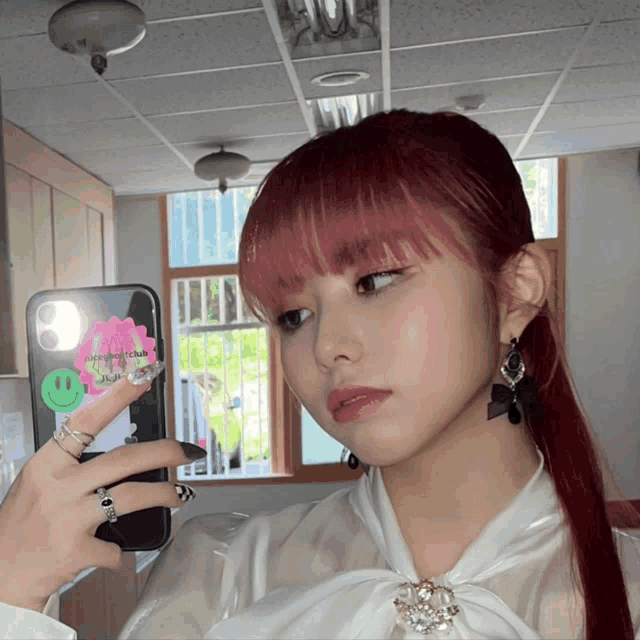 a girl with red hair is taking a selfie with a phone that has a smiley face