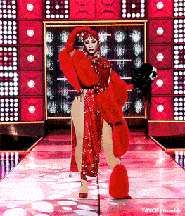 a drag queen is walking down the runway wearing a red fur coat and gloves .