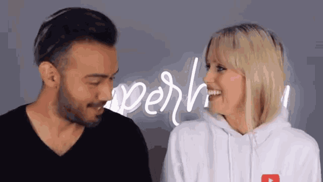 a man and a woman are looking at each other in front of a neon sign that says " yeah "