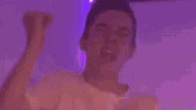 a young man is dancing in a room with purple lights behind him .