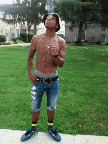 a shirtless man is smoking a cigarette while wearing a hat
