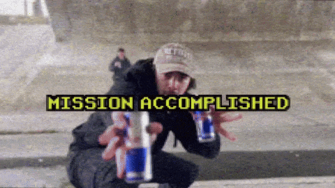 a man is holding two cans of red bull in front of a mission accomplished sign