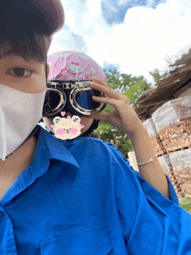 a man wearing a blue shirt and a white mask holds a pair of goggles