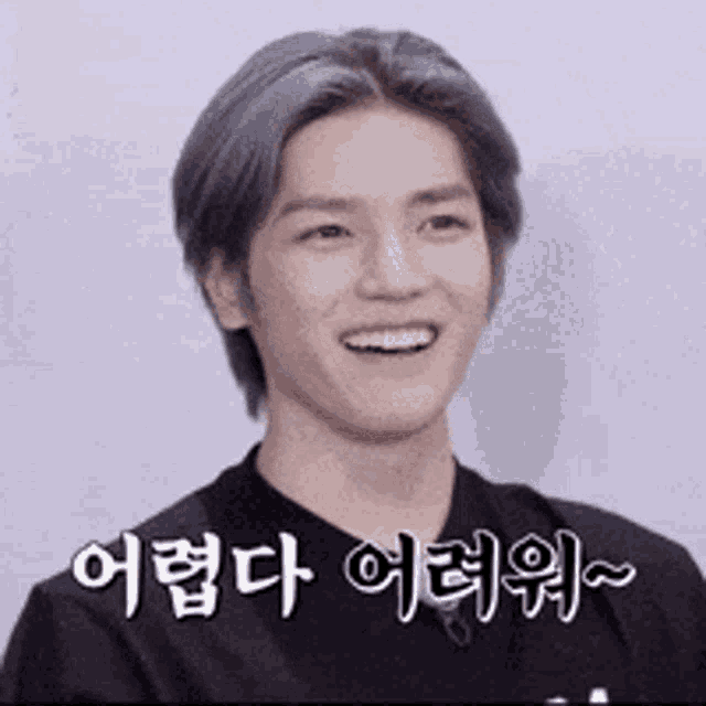 a young man with gray hair is smiling in a black shirt with korean writing on it .