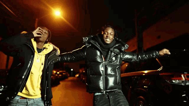 two men standing next to each other on a street at night