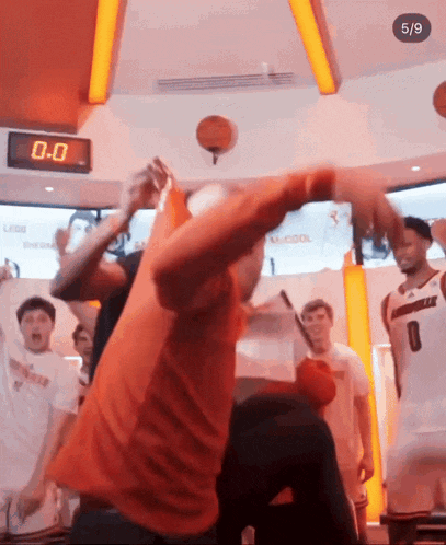 a man in an orange shirt is throwing a basketball in the air in front of a clock that says 0-0