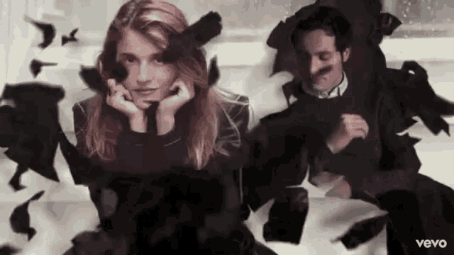 a man and a woman are sitting next to each other in a room surrounded by black feathers .