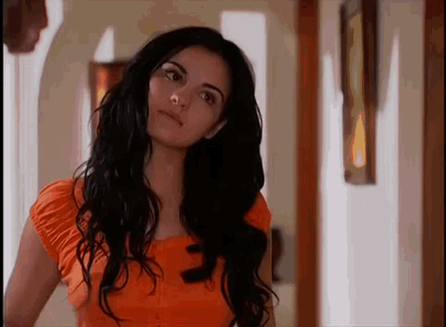 a woman with long black hair is wearing a bright orange top .