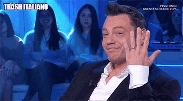 a man with a ring on his finger is sitting in front of a sign that says trash italiano on it
