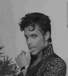 a black and white photo of a man with curly hair wearing a jacket and a watch .