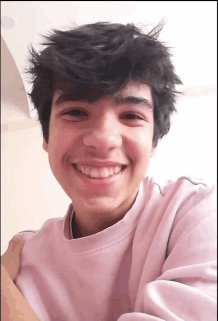 a young man wearing a pink shirt is smiling for the camera