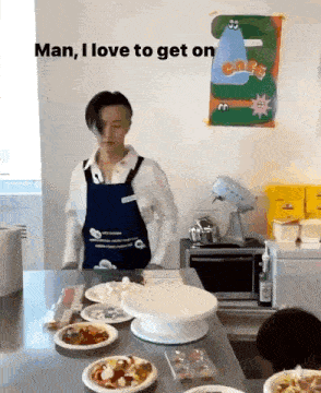 a man in an apron is standing in front of a table with plates of food and a cake on it .