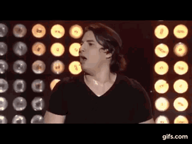 a man in a black shirt is standing in front of a row of lights .
