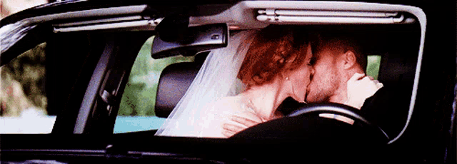 a bride and groom kissing in a car with the bride wearing a veil