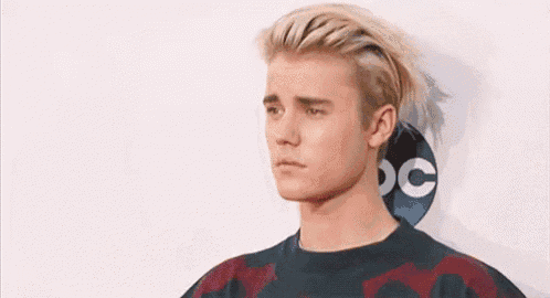 a young man with blonde hair is wearing a sweater and looking at the camera .