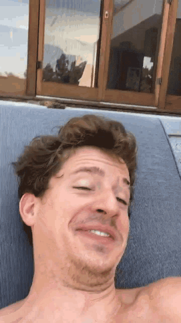 a man without a shirt is laying on a chair and making a funny face