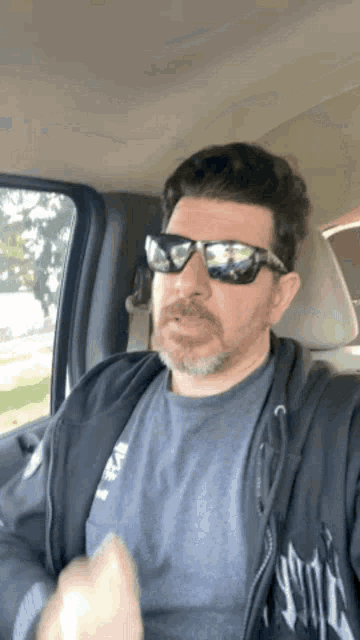 a man wearing sunglasses and a hoodie is sitting in the back seat of a car