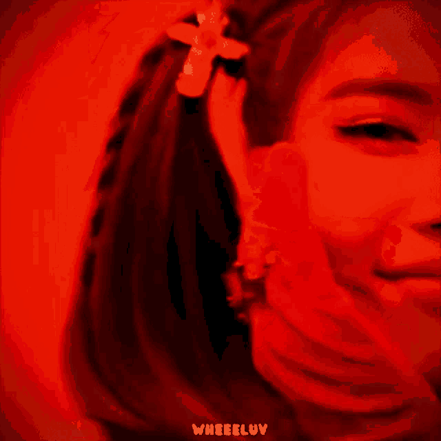 a woman 's face is being held in a red light and the word wheeluv is on the bottom of the image