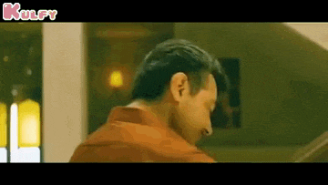 a man in a red shirt is standing in a room looking down .