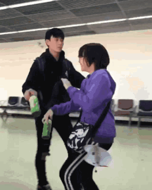 a woman in a purple sweatshirt is dancing with a man in a black jacket